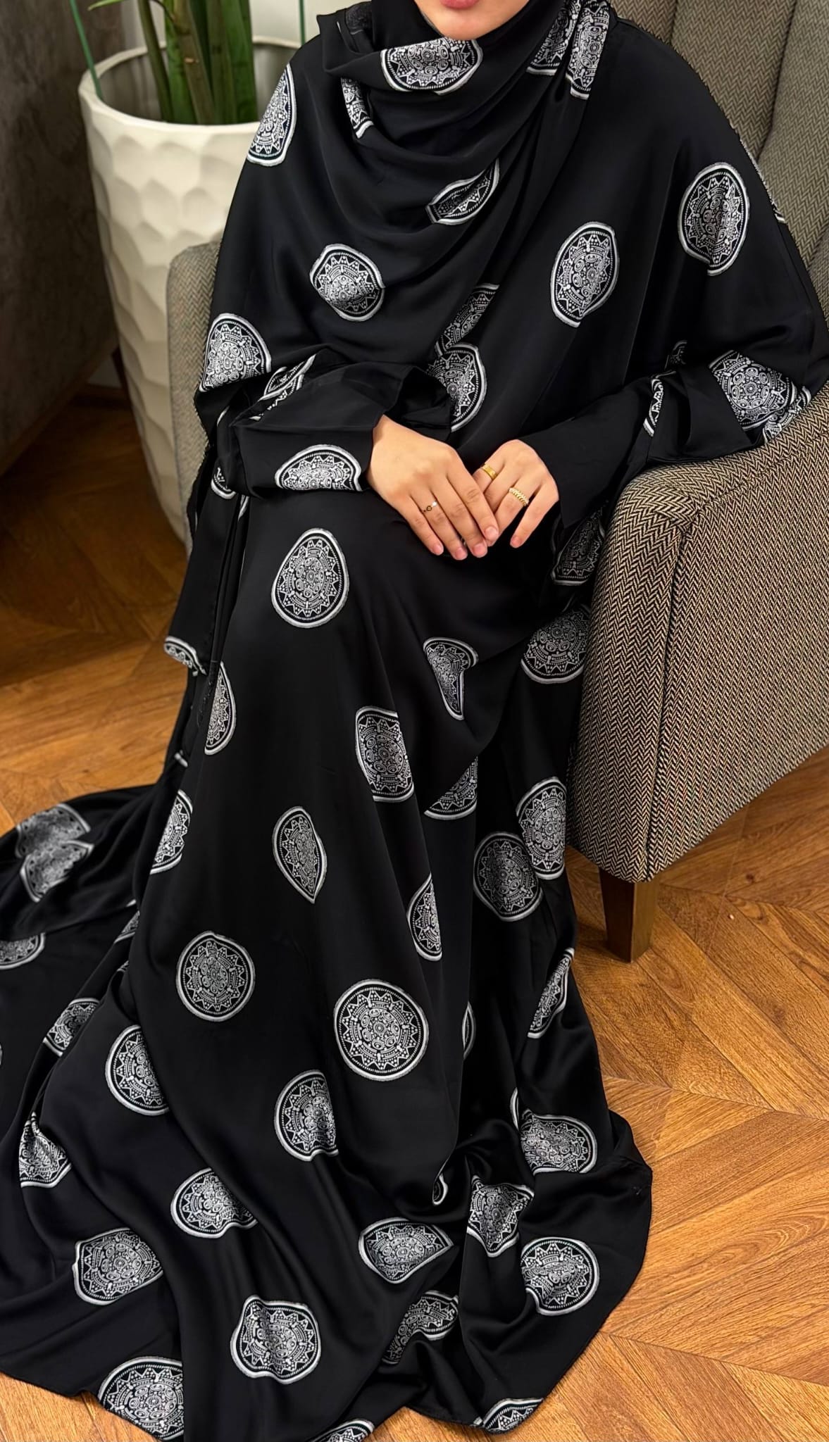 Sitzende Frau im schwarzen Abaya Set Mahira mit silberfarbenen Ornamenten und weit fallendem Butterfly-Schnitt.