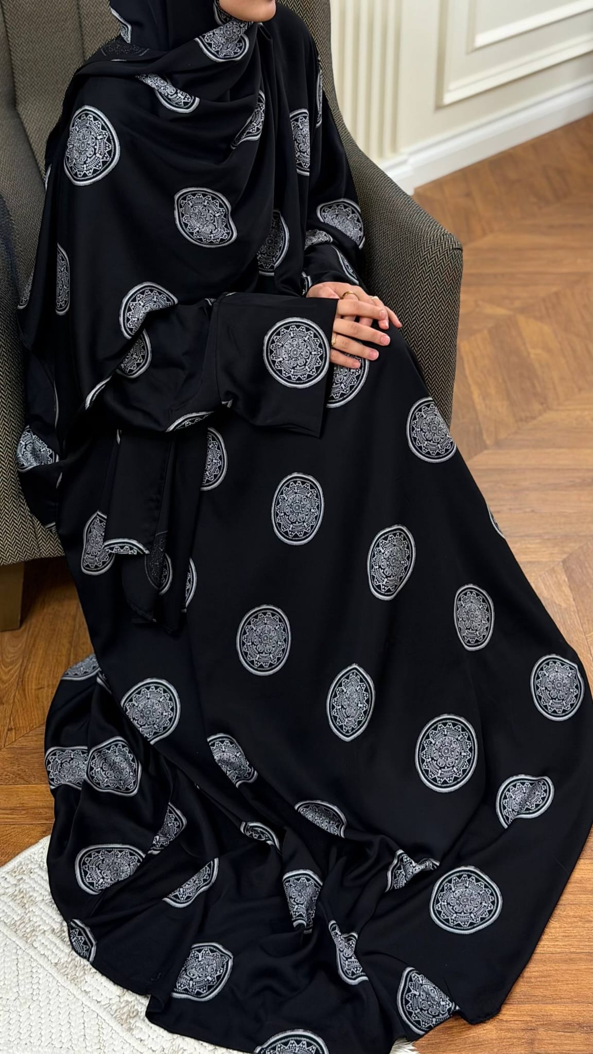 Schwarzes Butterfly Abaya Set Mahira im Sitzen mit locker fallendem Stoff, weiten Ärmeln und silberfarbenen Mustern.